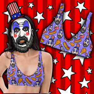 May include: A lilac-colored crop top with a repeating pattern of a clown face, hot dogs, fried chicken, and cupcakes. The clown face wears a patriotic top hat. The background is red with white stars and stripes.