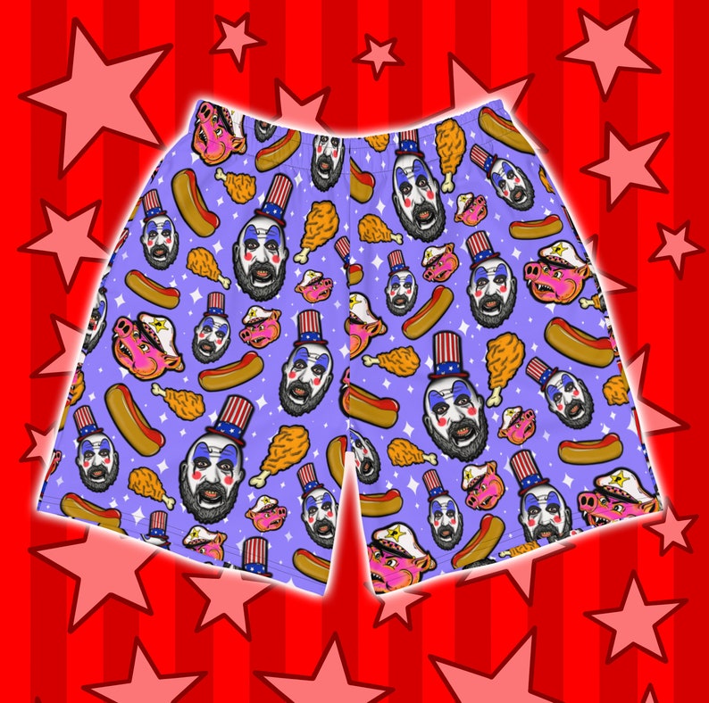 May include: Purple men's swim trunks with a repeating pattern of a man with a beard wearing a red, white, and blue hat, hot dogs, fried chicken, and pigs.