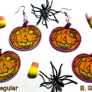 Könnte beinhalten: Zwei Paar Halloween-Ohrringe in Kürbisform. Ein Paar ist ein normaler Kürbis mit einem geschnitzten Gesicht und das andere Paar ist ein Glitzerkürbis mit einem geschnitzten Gesicht. Beide Paare haben einen rosa Hintergrund und den Text "Haddonfield 1978 Boogeyman" darauf.