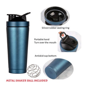 Puede incluir: Una botella de batidora de acero inoxidable azul con una tapa negra y una bola de batidora de metal. La botella tiene un asa de transporte y un fondo antideslizante. La tapa tiene un sello de silicona.