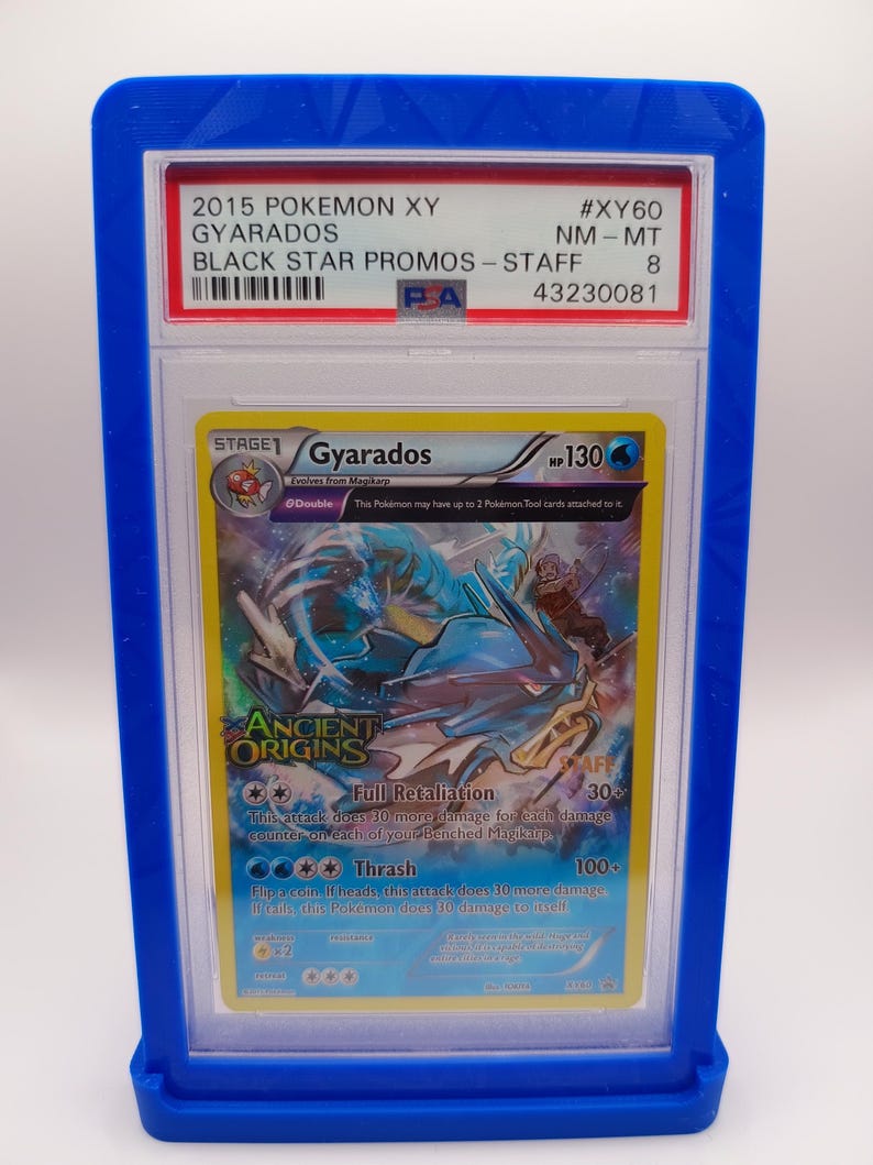 May include: A PSA graded Pokemon card in a blue plastic case. The card is a Gyarados from the Ancient Origins set. The card is graded NM-MT 8 and has the number #XY60. The card is a Black Star Promo - Staff card.