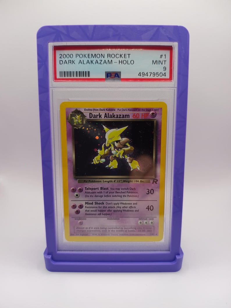 May include: A graded Pokemon card in a protective case. The card is a holographic Dark Alakazam from the Rocket set. The card is in mint condition and has a grade of 9. The card's number is #1. The card's text reads "Evolves from Dark Kadabra. Put Dark Alakazam on the Stage 1 card. Dark Alakazam 60 HP.  ... Teleport Blast You may switch Dark Alakazam with 1 of your Benched Pok&eacute;mon. (Do the damage before switching the Pok&eacute;mon.) Mind Shock Don't apply Weakness and Resistance for this attack. (Any other effects that would happen after applying Weakness and Resistance all happen.)"