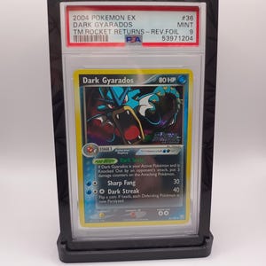 May include: A graded Pokemon card in a protective case. The card is a Dark Gyarados from the 2004 Pokemon EX: Team Rocket Returns set. The card is in mint condition and has a 9 out of 10 rating. The card features a dark blue and red Gyarados with a dark blue background. The card text reads "Dark Scale" and "Dark Streak".