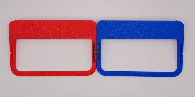 May include: Two plastic frames, one red and one blue, with a rectangular opening in the centre. The frames are textured and have a slightly raised edge.