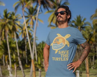 May include: A light blue t-shirt with a turtle graphic and the text "SAVE THE TURTLES". The graphic includes a turtle, palm trees, and waves. The background features palm trees and a blue sky.