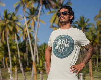 May include: A light-colored t-shirt with the text "TWENTY THOUSAND LEAGUES UNDER THE SEA" in a circular design. The shirt is worn outdoors with palm trees in the background.