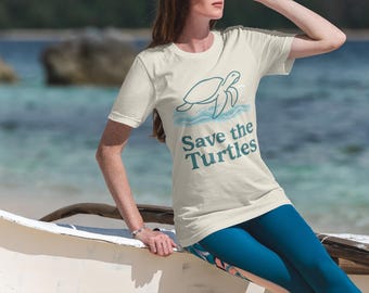 May include: Cream-colored t-shirt with a teal turtle graphic and the text "Save the Turtles." The shirt is paired with blue leggings. The image is set against a blurred beach background.