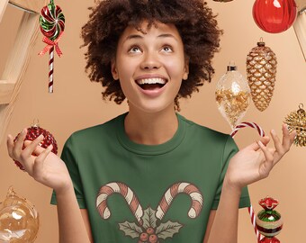 May include: A woman wearing a green t-shirt with a candy cane graphic, surrounded by Christmas ornaments. The ornaments are various colors and shapes, including red, gold, and green. The woman is wearing reindeer antlers.