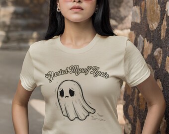 May include: Cream-colored t-shirt featuring a sad ghost graphic and the text "Ghosted Myself Again" in a script font. The ghost has a simple, cartoonish design with a downturned mouth and eyes. The shirt is a crew neck.