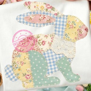 May include: White fabric with a patchwork bunny design. The bunny is made of various patterned fabrics, including floral, gingham, and polka dots. The design is in pastel colors, with pink, yellow, and blue accents. The design is stitched onto the fabric.
