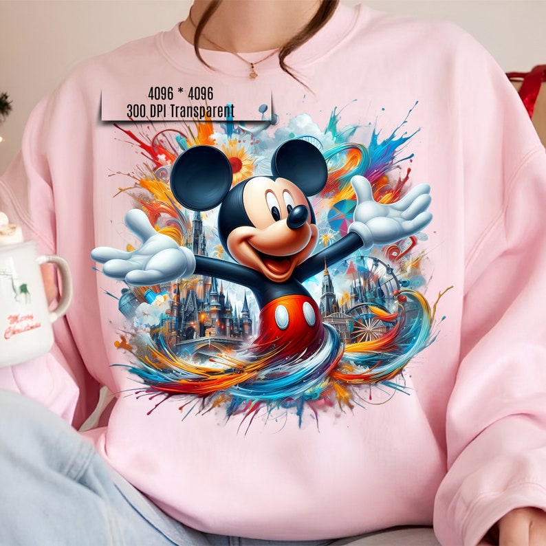 May include: A pink sweatshirt with a colorful graphic of Mickey Mouse in front of a cartoon cityscape. The graphic includes a colorful paint splatter effect.