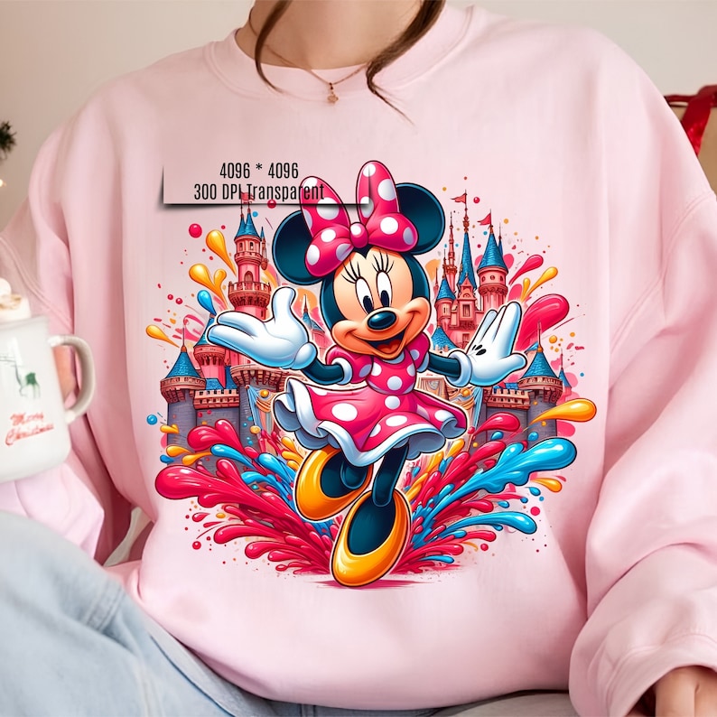 May include: Pink sweatshirt with a colorful graphic of Minnie Mouse in front of a castle. The graphic includes splashes of paint in red, blue, yellow, and orange.