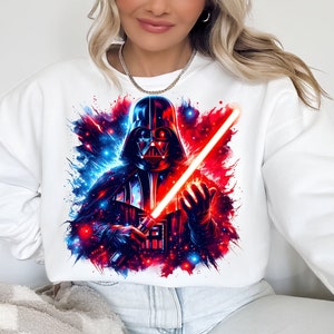May include: White sweatshirt with a colorful graphic print of Darth Vader holding a red lightsaber. The background is a galaxy with blue and red colors.
