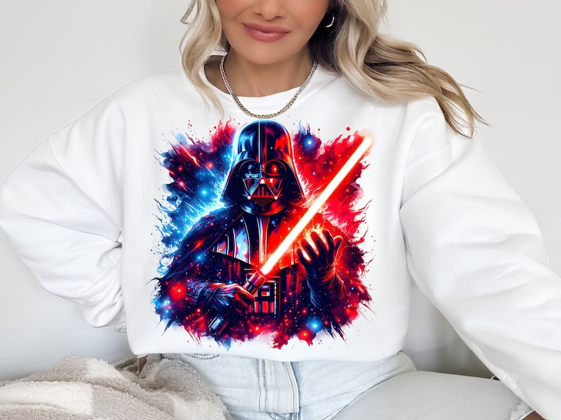 May include: White sweatshirt with a colorful graphic print of Darth Vader holding a red lightsaber. The background is a galaxy with blue and red colors.