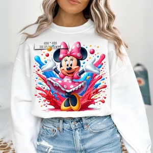 May include: White sweatshirt with a colorful graphic print of Minnie Mouse in a pink polka dot dress. The graphic features Minnie Mouse with a pink bow and surrounded by colorful paint splatters.