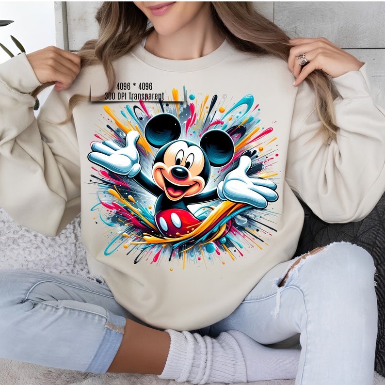 May include: A cream-colored sweatshirt with a colorful graphic print of Mickey Mouse. The graphic features Mickey Mouse with his arms outstretched, surrounded by colorful paint splatters.