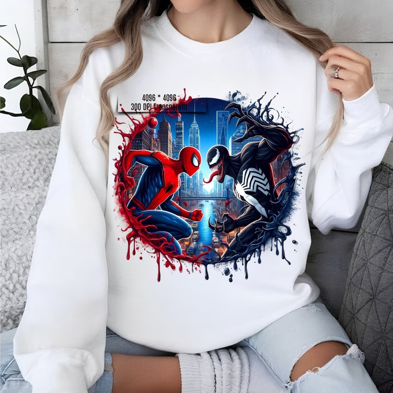 May include: White sweatshirt with a graphic print of Spider-Man and Venom fighting in front of a cityscape. The graphic is surrounded by red and black splatters of paint.