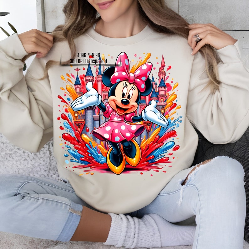 Puede incluir: Sudadera beige con un gr&aacute;fico colorido de Minnie Mouse con un vestido y lazo rosa de lunares, con un fondo de castillo. El dise&ntilde;o incluye vibrantes salpicaduras de rojo, naranja, amarillo y azul. El texto "4096 * 4096 300 DPI Transparent" es visible.