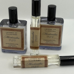 May include: A selection of Layerz of Illusions Marshmallow Puff perfume bottles. The clear bottles have black caps and brown labels. The labels state "Marshmallow Puff, Marshmallow, Vanilla, and Sugar."
