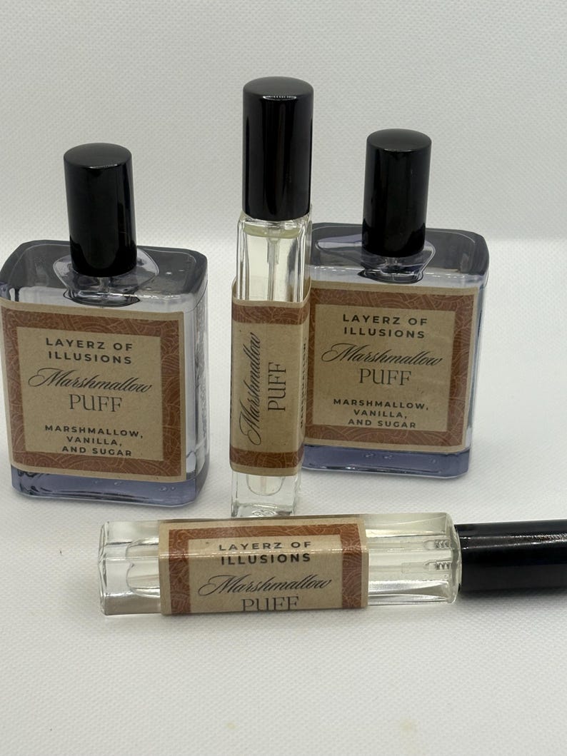 May include: A selection of Layerz of Illusions Marshmallow Puff perfume bottles. The clear bottles have black caps and brown labels. The labels state "Marshmallow Puff, Marshmallow, Vanilla, and Sugar."