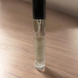 Puede incluir: Una botella de vidrio transparente con una tapa negra y una etiqueta blanca que dice "DIVINE CLOUDS".