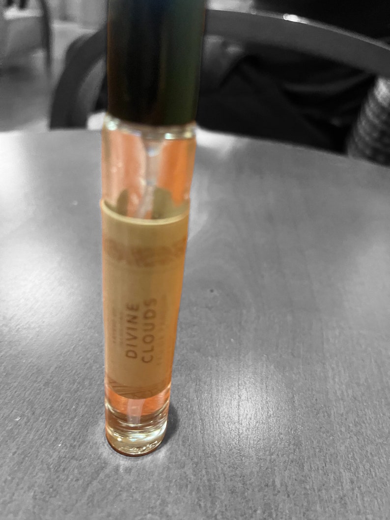 Puede incluir: Una botella de vidrio transparente con una tapa negra y una etiqueta que dice "DIVINE CLOUDS". La botella est&aacute; llena de un l&iacute;quido naranja claro.
