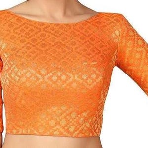 Puede incluir: Blusa naranja con cuello barco y mangas tres cuartos. La tela tiene un patrón geométrico texturizado. La parte superior es de color naranja liso y parece estar hecha de un material tejido.