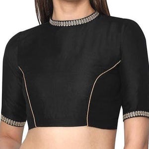 Może przedstawiać: Czarna bluzka z krótkim rękawem i wysokim dekoltem. Bluzka posiada złote wykończenia wzdłuż szwów, dekoltu i mankietów. Tkanina jest gładka, w jednolitym kolorze.