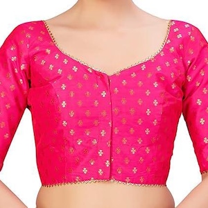 Pode incluir: Uma blusa rosa vibrante com mangas três-quartos e decote em V. O tecido é adornado com um sutil padrão floral dourado. As bordas das mangas e decote são aparadas com uma delicada borda dourada.
