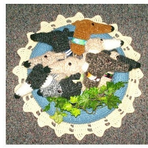 Puede incluir: Un grupo de perros galgos de crochet en varios colores, incluyendo marr&oacute;n, negro y blanco, est&aacute;n dispuestos en un c&iacute;rculo sobre un encaje de crochet azul y blanco. Los perros est&aacute;n todos mirando hacia afuera, y hay hojas verdes en el centro del c&iacute;rculo.