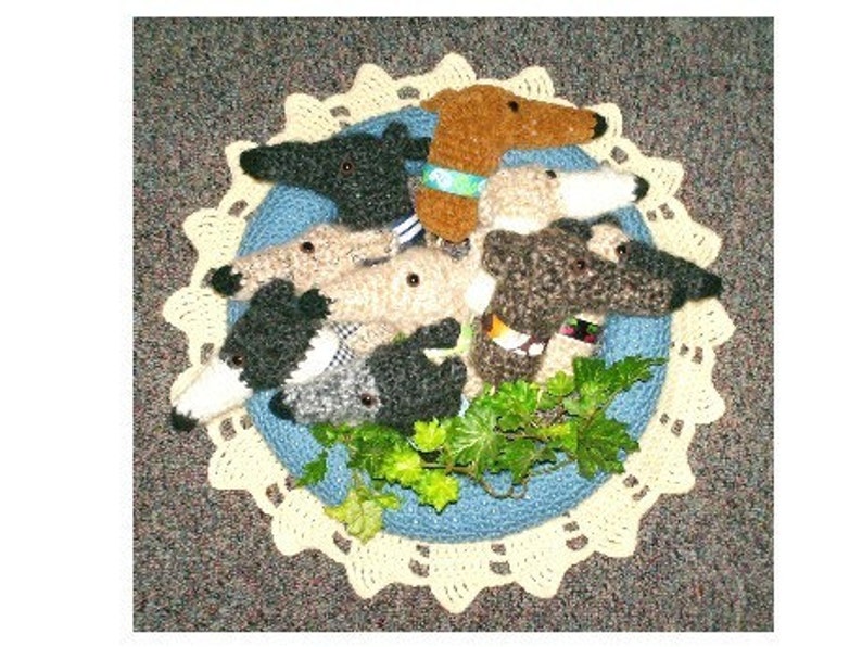 Puede incluir: Un grupo de perros galgos de crochet en varios colores, incluyendo marr&oacute;n, negro y blanco, est&aacute;n dispuestos en un c&iacute;rculo sobre un encaje de crochet azul y blanco. Los perros est&aacute;n todos mirando hacia afuera, y hay hojas verdes en el centro del c&iacute;rculo.