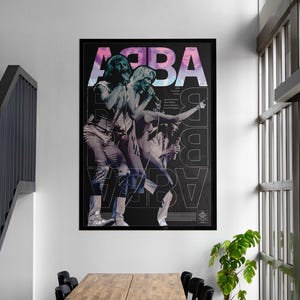 May include: A rectangular wall poster featuring the band ABBA in a black and white performance photograph. The word ABBA is printed in large, stylised, gradient-coloured letters at the top. The design includes repeating vertical text and a dark background.