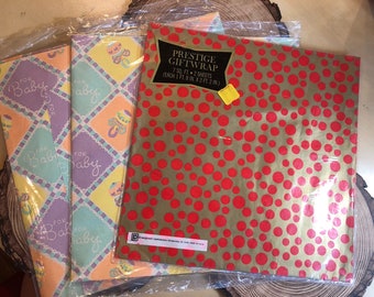 May include: Three rolls of baby themed gift wrap. Two rolls have a checkered pattern with the words "For Baby" in purple, green, and yellow. The third roll has a gold background with red polka dots. The text on the packaging reads "Prestige Giftwrap 7 sq. ft. - 2 sheets (each 1 ft. 8 in. x 2 ft. 2 in.)"