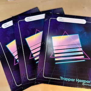 May include: Four Trapper Keeper portfolios with a retro design. The covers feature a geometric design with a pink and yellow gradient, a pink triangle, and the words "Trapper Keeper Portfolio". Each portfolio has a white label for name and subject.