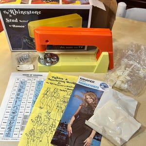 May include: Vintage Rhinestone & Stud Setter by Ronco, with orange and yellow plastic construction. Includes instruction booklets, rhinestones, and a box. The box reads "As seen on TV".