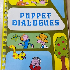 May include: A green book with a yellow spine and a spiral binding. The cover features a colorful illustration of puppets and the title "Puppet Dialogues: 24 Bible stories to be told with puppets". The book is by Charles E. Magnet and published by Accent Books.