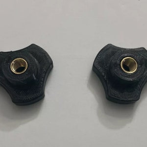 May include: Two black plastic knobs with a brass threaded insert. The knobs have a three-pronged design.