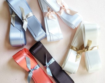 May include: Assortment of satin ribbon in various colors, including white, light blue, coral, and black. The ribbon is tied in bows with matching ribbon.