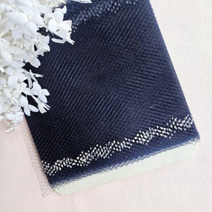 May include: A roll of navy blue tulle fabric with a white beaded trim. The fabric is on a white background.