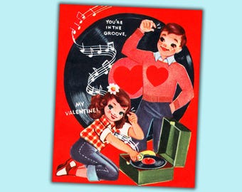May include: Vintage Valentine's Day card with a red background. A couple is depicted near a record player. The man wears a red sweater with a heart, and the woman is kneeling. Text reads "You're in the groove, My Valentine!"