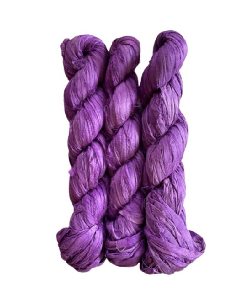 May include: Three skeins of purple silk ribbon, twisted together. The ribbon is made of thin, shredded silk and has a soft, textured look.