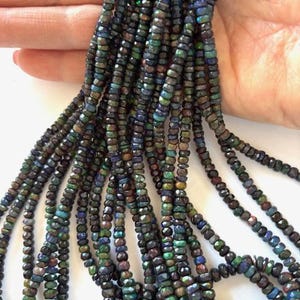 May include: A strand of black opal beads with a faceted, teardrop shape. The beads are iridescent with shades of green, blue, and purple.
