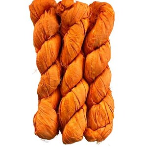 May include: A bundle of three twisted skeins of vibrant orange silk ribbon yarn. The material features a crinkled, textured surface with frayed edges along the length of the fabric strips, creating a voluminous and layered appearance in this yarn.