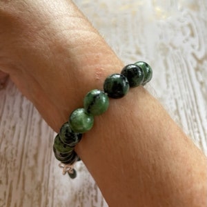 May include: A green and black gemstone bracelet with round beads. The bracelet is on a person's wrist.