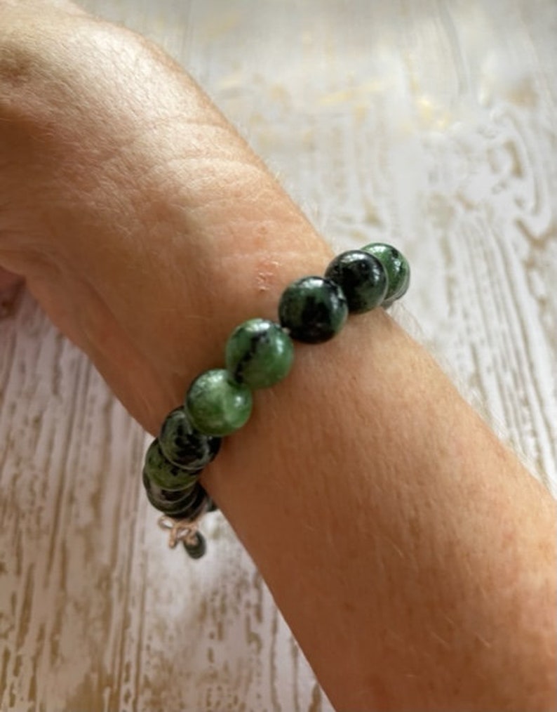 May include: A green and black gemstone bracelet with round beads. The bracelet is on a person's wrist.