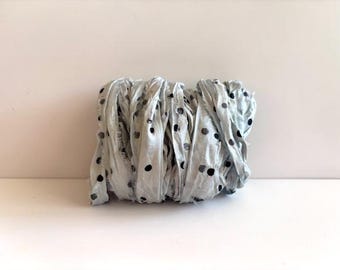 May include: A light blue scarf with black polka dots. The scarf is made of a soft, lightweight fabric and has a frayed edge. The scarf is folded and appears to be new.
