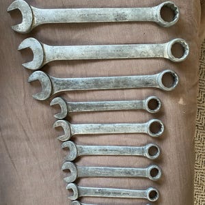May include: A set of well-used, silver-coloured spanners of different sizes, arranged in a descending order. Each spanner features an open end and a closed, circular end. The tools are made of metal and show signs of wear, indicating they are vintage.
