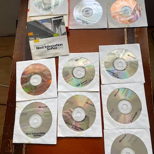 Può includere: Una collezione di CD software Microsoft, tra cui titoli come Commerce Server, Host Integration Server 2000 ed Exchange 2000. I CD sono in buste di carta bianca, con il logo Microsoft visibile. I dischi sono argentati e riflettono la luce.