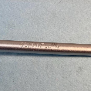 Op de afbeelding: Een zilveren dubbele ringsleutel met een 12-punts dopsleutelontwerp. De tool heeft een lange, slanke behuizing met tekst in het metaal geëtst. De sleutel is ontworpen voor het aandraaien of losdraaien van moeren en bouten.