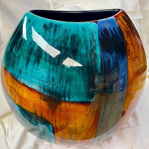 Könnte beinhalten: Eine große, runde dekorative Vase mit glänzendem Finish. Die Vase hat ein Farbblock-Design mit Türkis-, Orange-, Blau- und Brauntönen. Silberblatt-Akzente sind über dem türkisfarbenen Bereich verstreut. Der Innenraum ist schwarz.